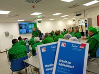 Mitarbeitende in grünen T-Shirts bei einer Betriebsversammlung in einem Konferenzraum